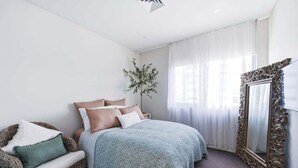 A bedroom with a bed, a chair, a mirror, and a plant. - Kai - Penthouse Luxury with breathtaking Ocean views (Coffs Harbour)