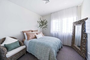 Ein Schlafzimmer mit einem Bett, einem Sessel, einem Spiegel und einer Pflanze.