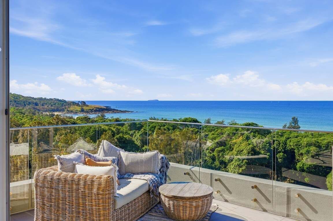 A balcony with wicker furniture overlooking a coastal landscape.