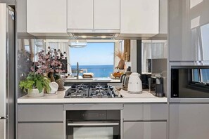 A modern kitchen with a gas stove, oven, and a view of the sea. - Kai - Penthouse Luxury with breathtaking Ocean views (Coffs Harbour)