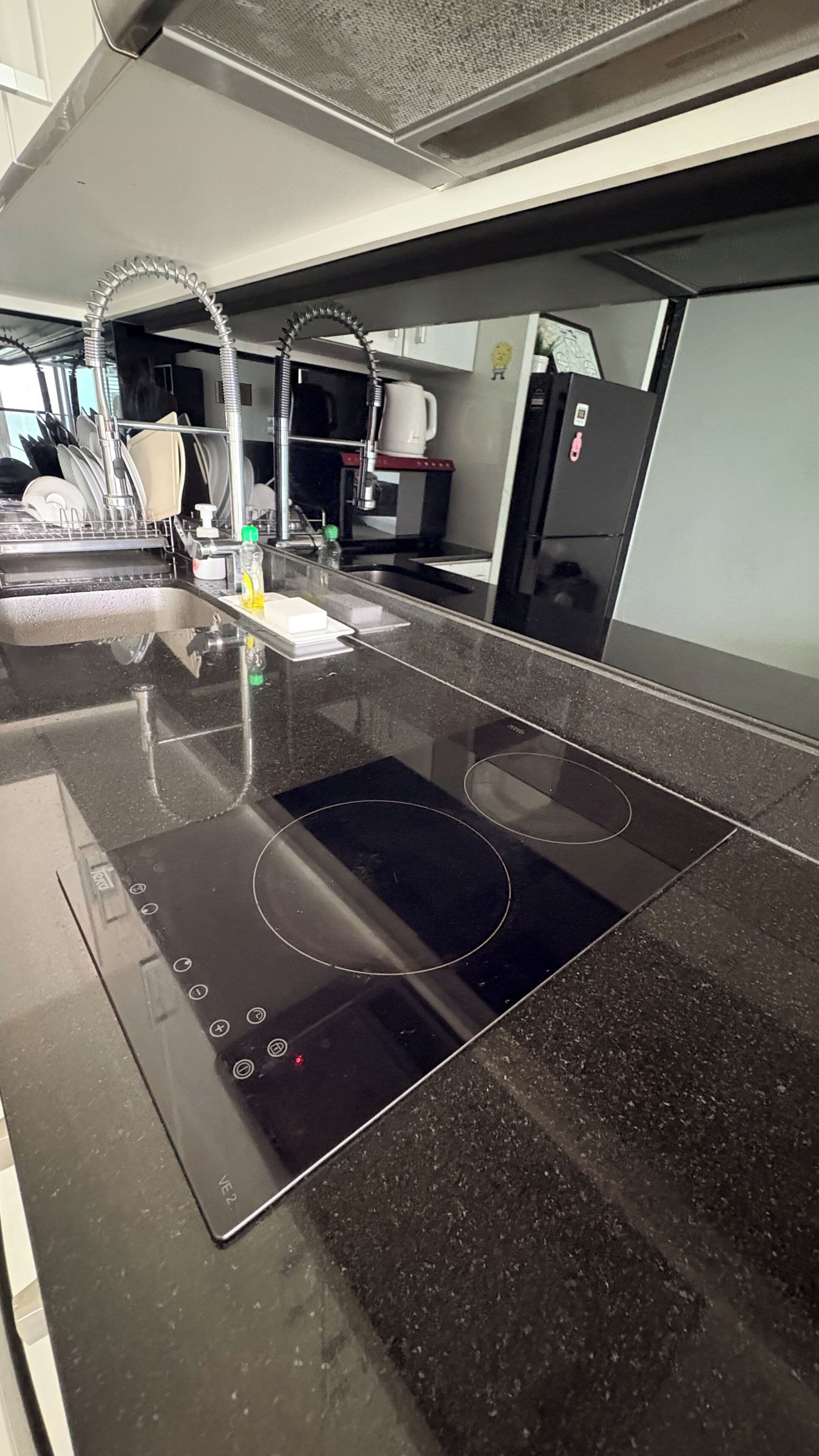 A kitchen with a black countertop, stainless steel sink, and an induction cooktop.