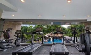 Une salle de sport équipée de tapis de course, de vélos d’appartement et d’une piscine avec vue sur une cascade.