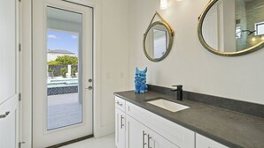 Um banheiro com porta branca, pia, espelho e um objeto decorativo azul no balcão.