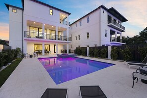 Ein modernes, zweistöckiges Haus mit Swimmingpool, Sitzgelegenheiten im Freien und einem gepflegten Garten.