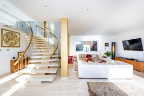 Ein modernes Wohnzimmer mit einem weißen Sofa, einem großen Flachbildfernseher und einer Treppe mit Holzgeländer.