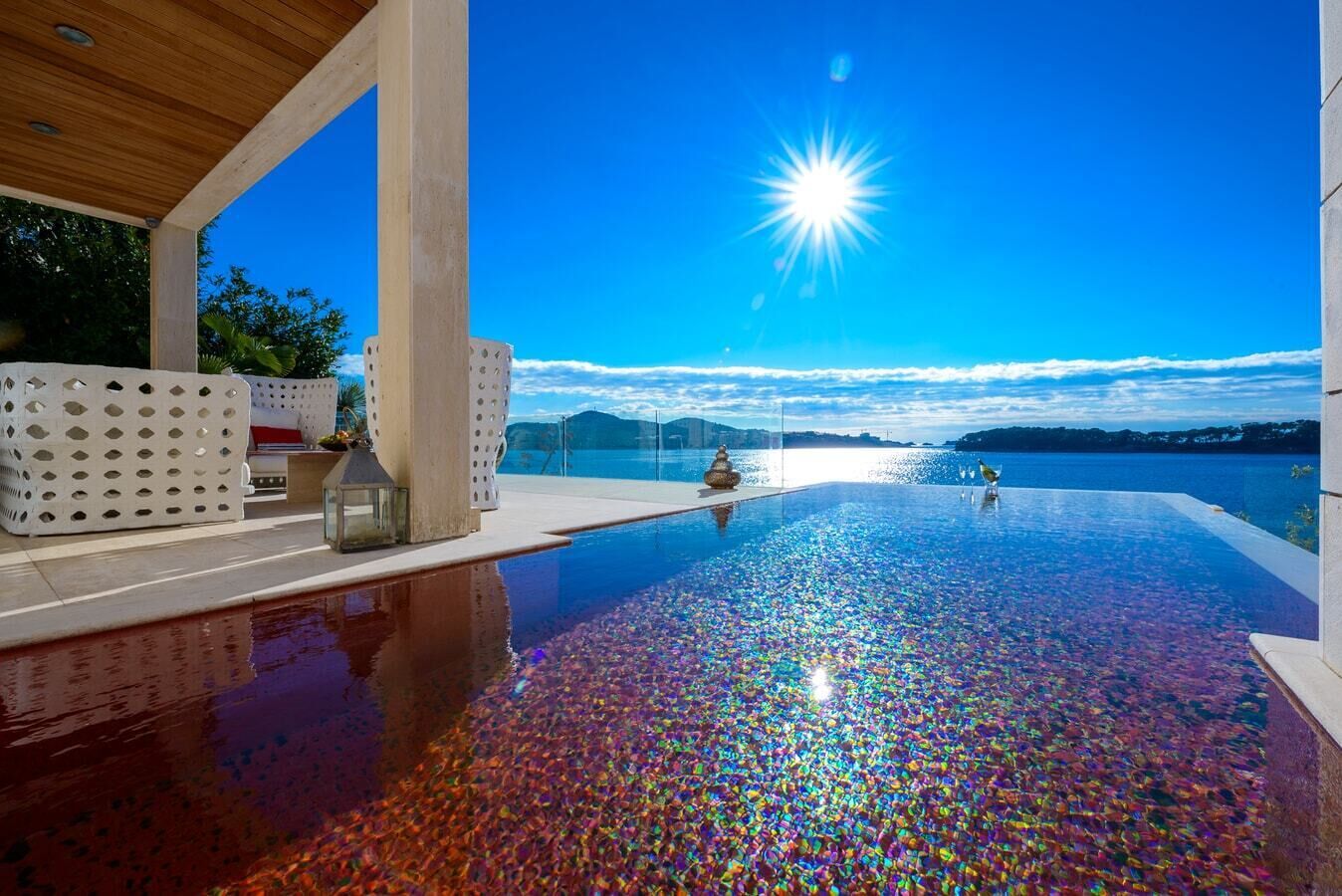 Une piscine à débordement offrant une vue dégagée sur l’horizon et les montagnes, un plafond en bois et un espace extérieur aménagé avec des sièges blancs.