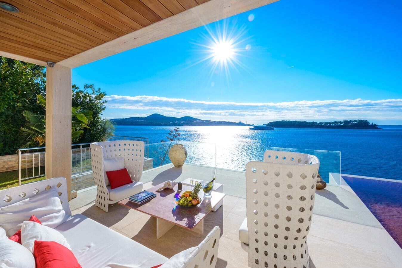 A terrace with white furniture, a table with a fruit bowl, and a view of the sea.