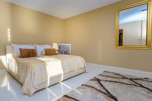 Ein Schlafzimmer mit einem Bett, Kissen, einem Teppich und einem gerahmten Bild an der Wand.