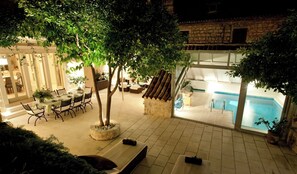 Ein Poolbereich im Innenbereich mit Steinwand, ein Essbereich mit Tisch und Stühlen sowie eine Lounge mit einer Couch und einem kleinen Tisch.