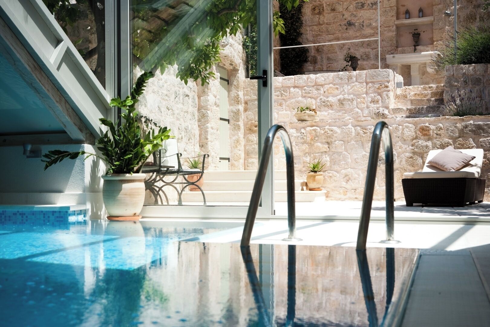 A pool area with a clear view of the water, a potted plant, and a stone wall in the background.