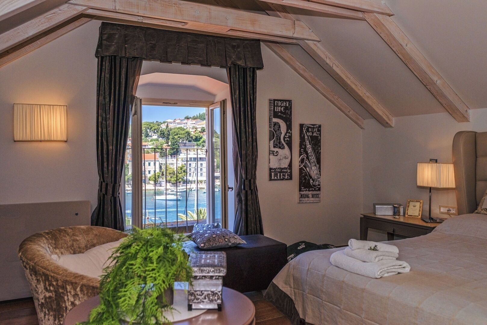 A hotel room with a bed, a chair, a small table, a lamp, and a view of the sea.