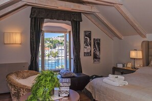 Una camera d'albergo con un letto, una sedia, un tavolino, una lampada e vista sul mare.