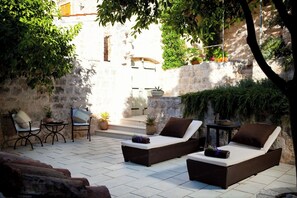 Ein sonniger Außenbereich mit Korlounge-Stühlen und einem kleinen Tisch, umgeben von Topfpflanzen und einer Steinmauer.