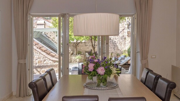 A dining area with a table, chairs, a vase of flowers, and a view through a glass door to an outdoor seating area. - Villa Ljuba - Private villa with pool, Hvar (Hvar)
