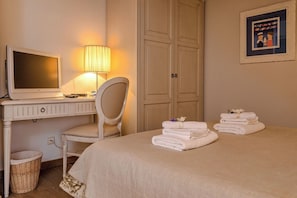 A hotel room with a bed, a desk with a computer, a chair, a wardrobe, and a framed picture on the wall.