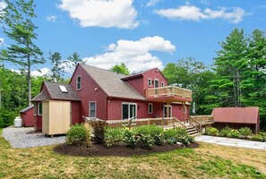 Een rood huis met twee verdiepingen, een balkon, een tuinhuisje en een overdekte veranda.