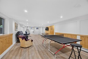 A room with a ping pong table, a cushioned chair, and a wooden cabinet. - Family Friendly Home Just Minutes from Boothbay Harbor! (Boothbay)