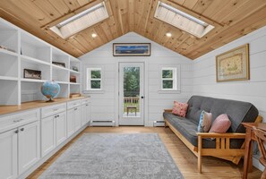A cozy room with a lofted ceiling, a gray sofa with cushions, a wooden side table, and a globe on a shelf. - Family Friendly Home Just Minutes from Boothbay Harbor! (Boothbay)