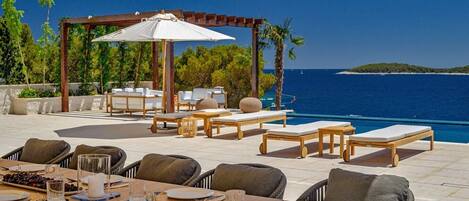 An outdoor dining area with a view of the sea, including tables, chairs, and umbrellas.