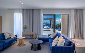 Ein modernes Wohnzimmer mit einem blauen Sofagarnitur, einem runden Couchtisch und Meerblick durch große Fenster.