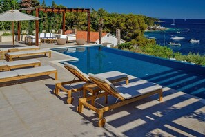 A poolside area with lounge chairs and a pergola, overlooking a coastal view with boats. - Villa Ulrika - Private villa with swimming pool (Hvar)