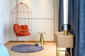 Ein Zimmer mit Hängesessel, einem kleinen runden Tisch, einem Beistelltisch mit Lampe und einem blauen Vorhang.