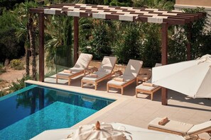 Un espace aménagé au bord de la piscine, avec des chaises longues et un parasol, le tout entouré de verdure.