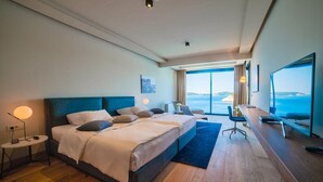 Een hotelkamer met een groot bed, een bureau en uitzicht op zee.