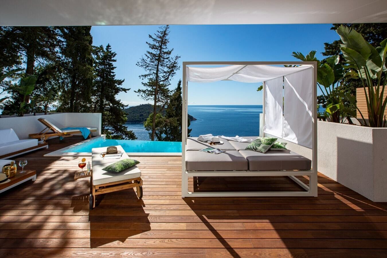 Un espace extérieur privé doté d’une piscine, de chaises longues et d’un lit à baldaquin offrant une vue sur la mer.
