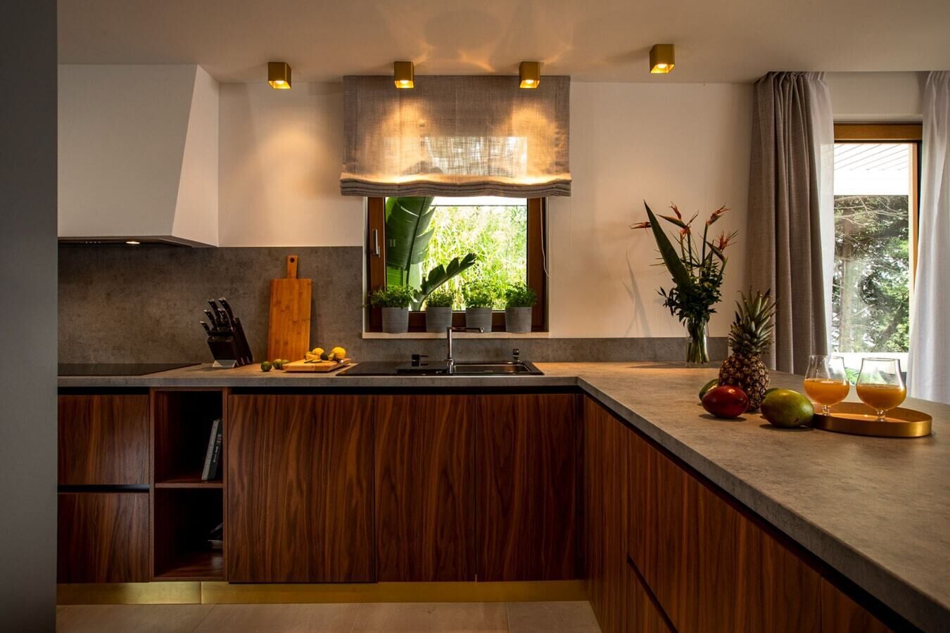 Une cuisine moderne dotée d’un îlot central en bois, de meubles de rangement intégrés et d’une fenêtre donnant sur un espace verdoyant.