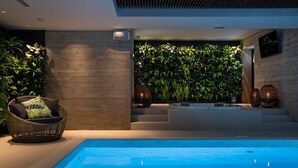 Un área de piscina interior moderna con zona de estar, una pared de vegetación y una escalera que lleva a un nivel superior.
