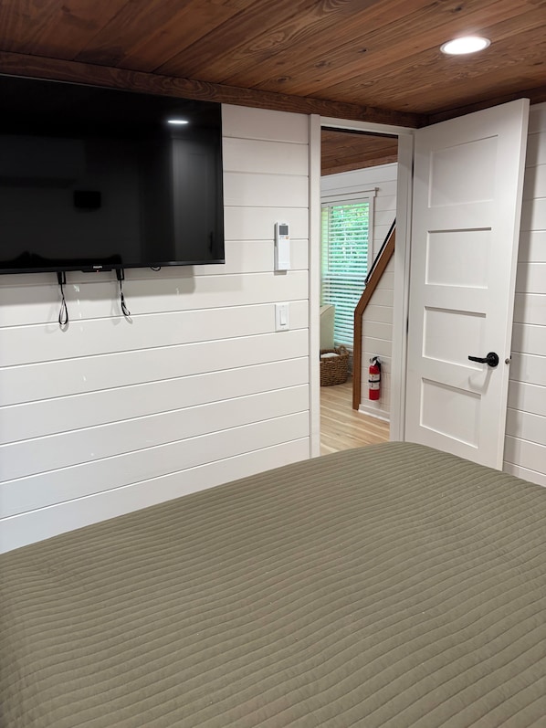 Una habitación con un televisor montado en la pared, una puerta que da a una escalera y un extintor en la pared.