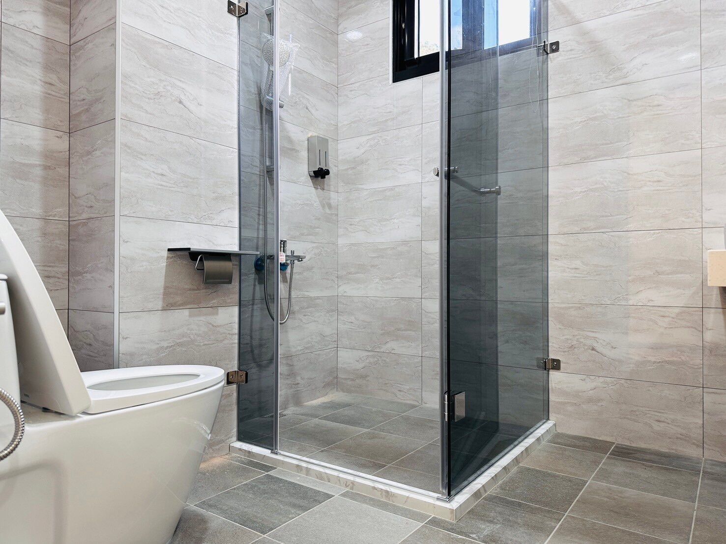 A modern bathroom with a glass-enclosed shower, a toilet, and a towel rack.