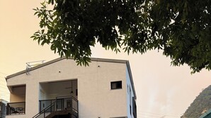 Un immeuble à plusieurs étages doté de balcons, d’un espace extérieur aménagé pour s’asseoir et offrant une vue sur une colline.