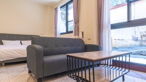 Une pièce comprenant un lit, un canapé gris, une petite table et une fenêtre avec des rideaux.