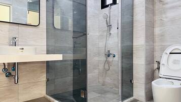 A modern bathroom with a glass-enclosed shower, a toilet, and a sink with a mirror above.