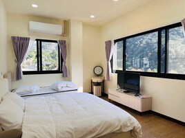 Un dormitorio con cama, televisor, mesita de noche y ventana con cortinas.