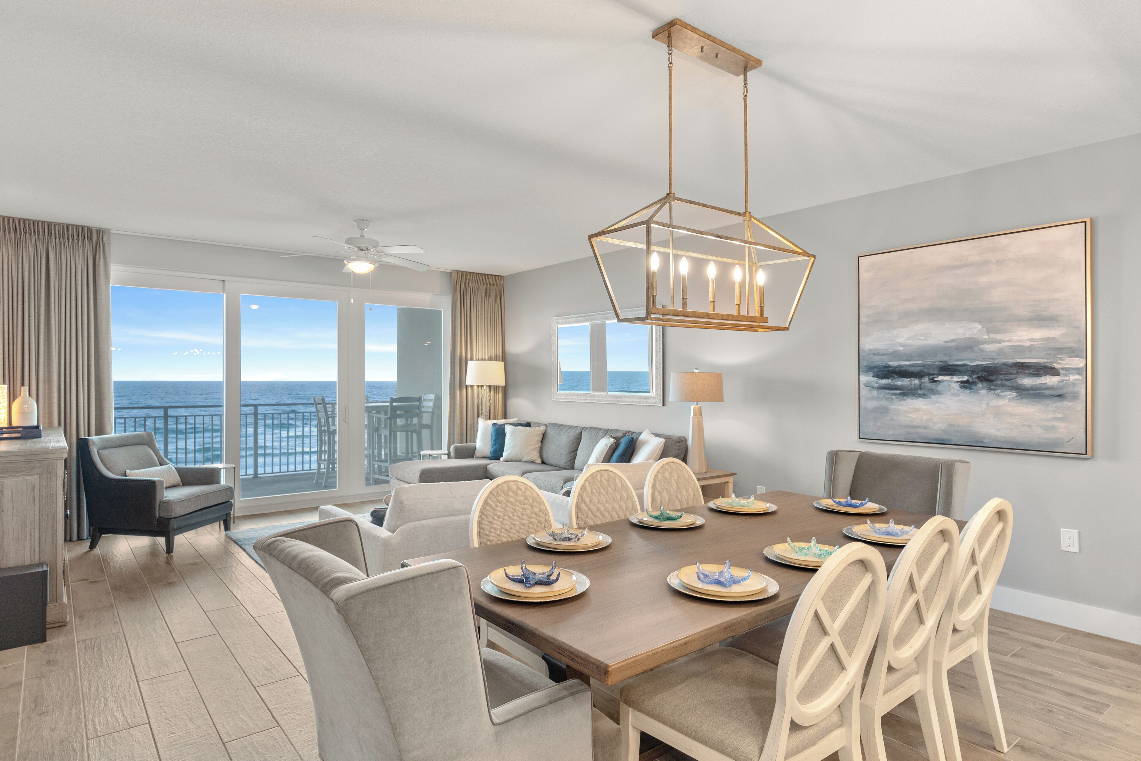 A modern living room with a dining area, large windows with a view of the ocean, and a ceiling fan.