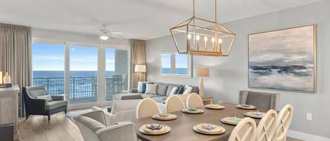 A modern living room with a dining area, large windows with a view of the ocean, and a ceiling fan.