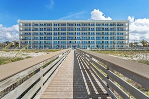 Eine lange Holzpromenade führt zu einem mehrstöckigen Hotel mit Balkonen.