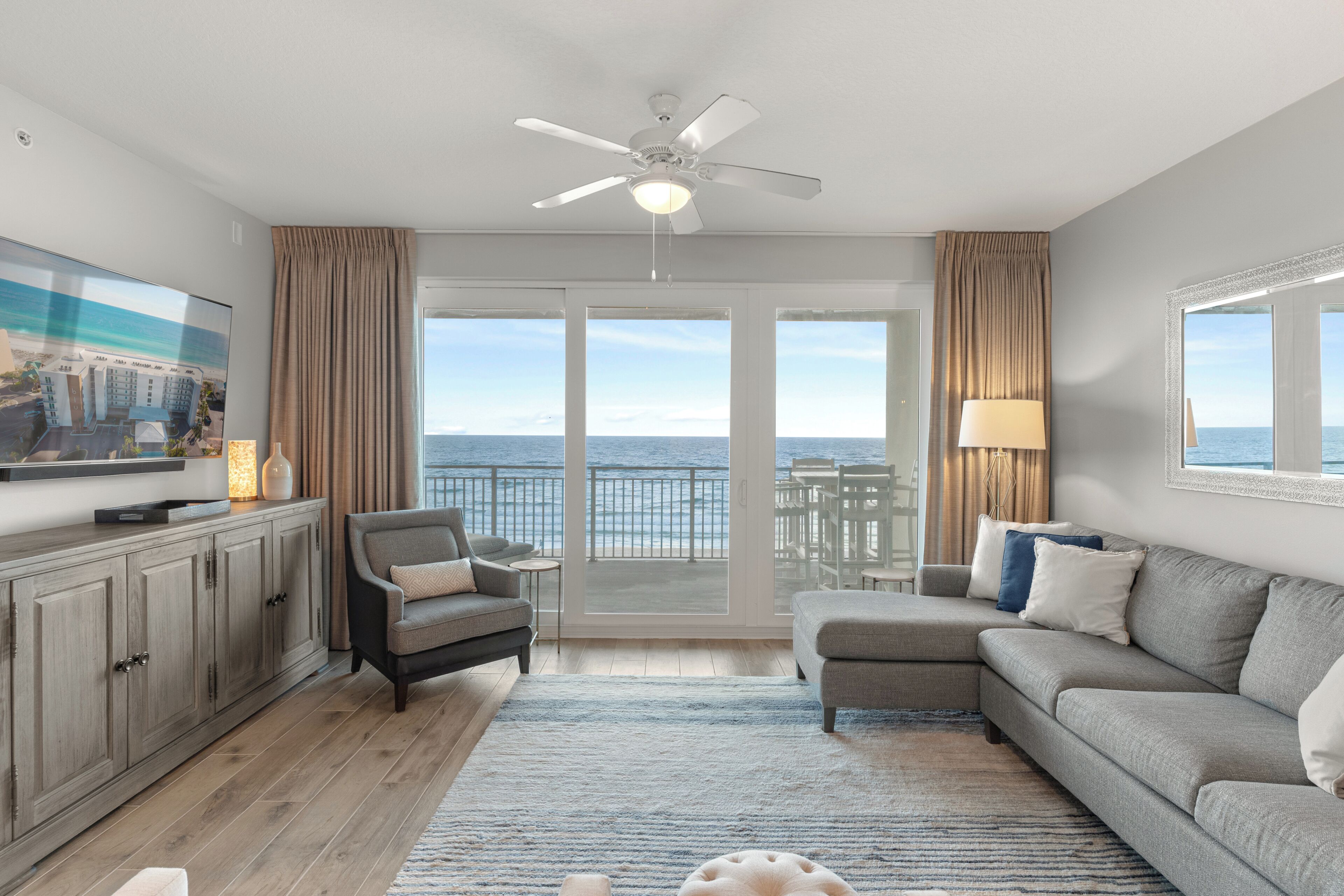 A modern living room with a balcony, a ceiling fan, and a view of the ocean.