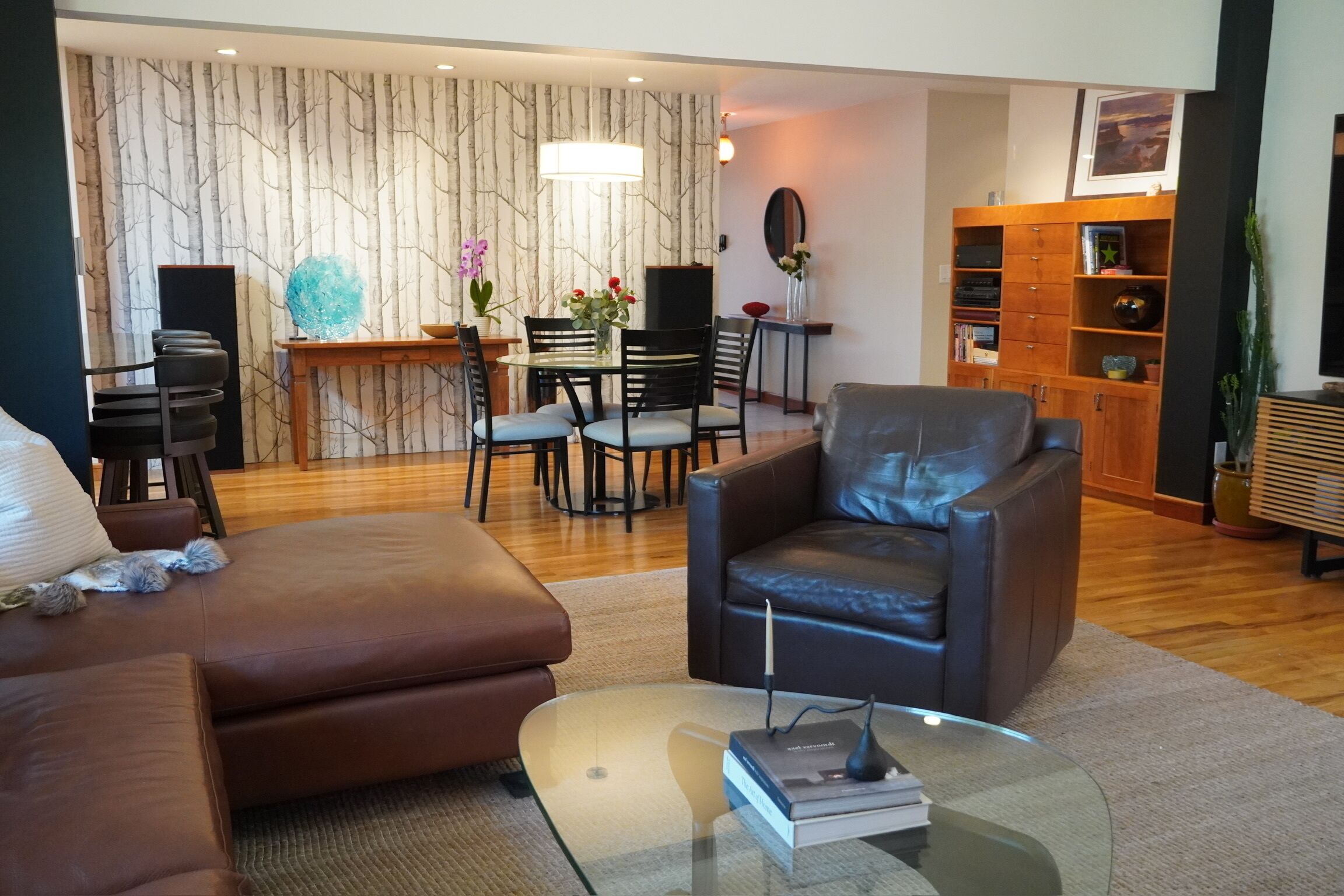 Un salon moderne avec un fauteuil en cuir, une table basse en verre et un coin repas comprenant une table et des chaises en bois.
