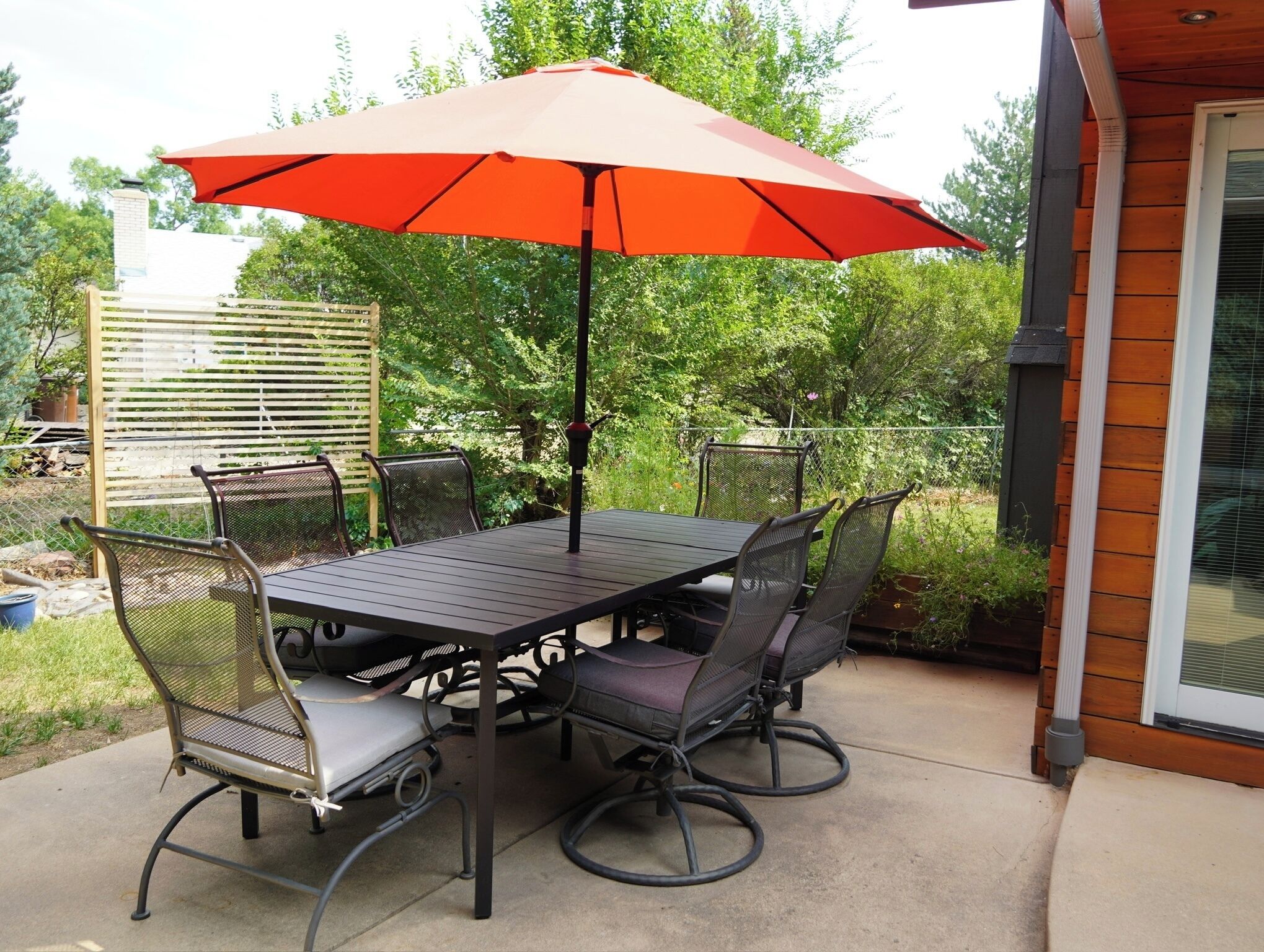 An outdoor patio with a table and chairs, an umbrella, and a wooden fence.