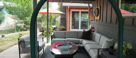 An outdoor patio with a curved ceiling, a sectional sofa, a glass-top coffee table, and a red umbrella.