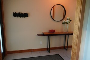 A hallway with a wooden console table, a black wall decoration, a round mirror, and a vase with white flowers. - Modern 3 bedroom in nice location.   Less than 2 miles to Downtown. (Boulder)