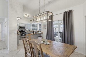 Une cuisine moderne avec des meubles blancs, une table à manger en bois et un luminaire suspendu.