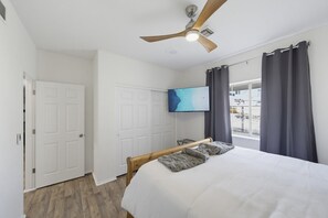 Une chambre à coucher avec un lit, un ventilateur de plafond, une télévision et une fenêtre avec des rideaux.