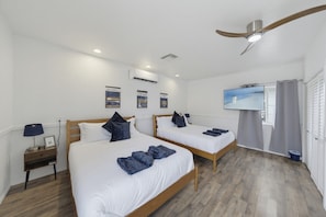 Ein Hotelzimmer mit zwei Betten, einem Deckenventilator, einem Fernseher und einem Fenster mit Vorhängen.