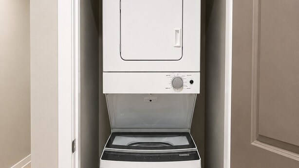 Een kleine, witte wasruimte met een ingebouwde wasmachine en droger, voorzien van een bedieningspaneel en een deur.