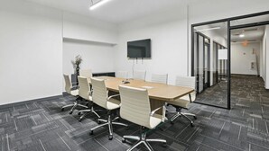 Een vergaderruimte met een lange tafel, witte stoelen, een flatscreen televisie en een glazen scheidingswand.